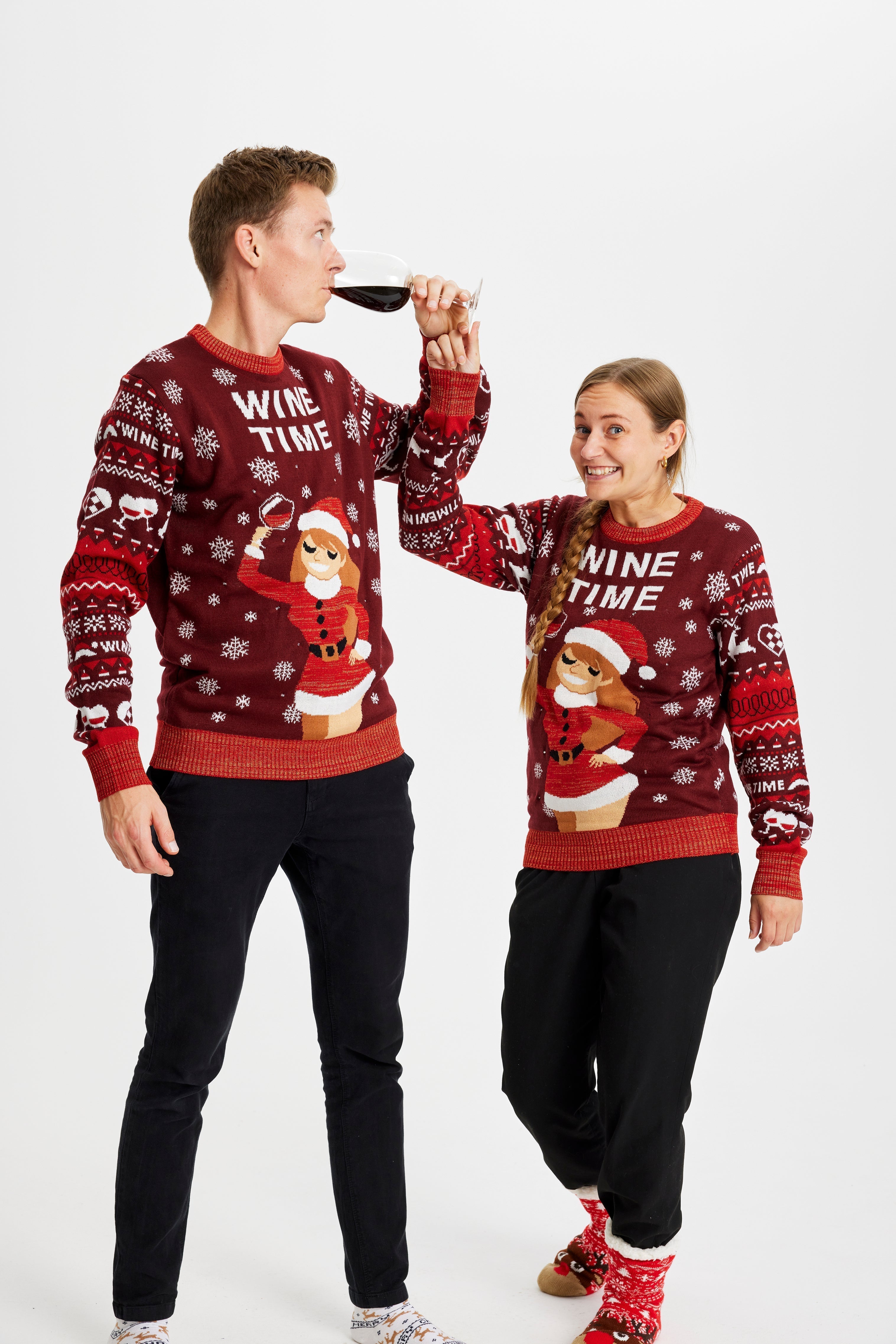 Un couple posant avec un verre de vin portant un pull rouge de Noël avec la citation